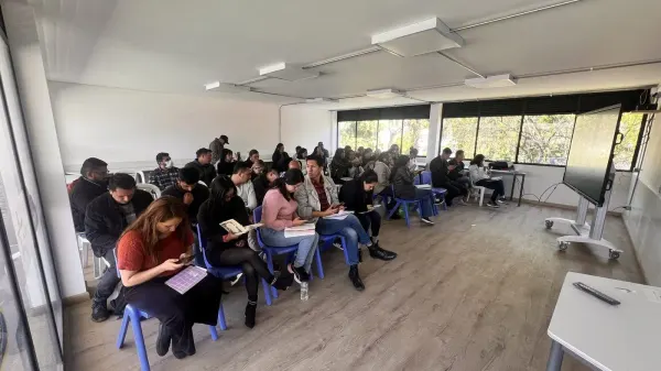 Adult students in a higher education room facing an interactive screen on a mobile stand