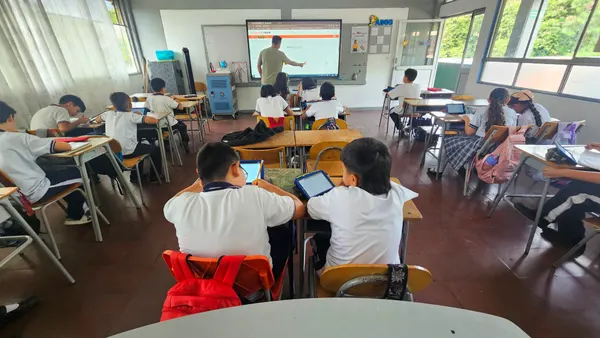 A teacher opens the eClass platform on the interactive screen while his students work with tablets and notebooks