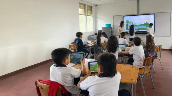 A student works on the interactive screen with a local landscape while the teacher accompanies her and the class follow from their tablets