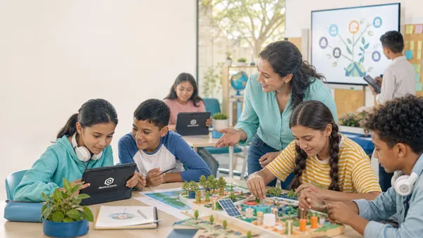 Students build a model of a sustainable town alongside their teacher and check their tablets